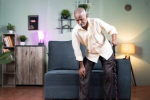 a mature African American man using a cane to get up from a couch