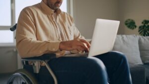 An older man in a wheelchair uses his laptop and researches the SSDI grid rules for ages 55-59