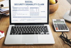 A laptop with a Social Security Disability claim form on the screen, with someone nearby wondering whether they can appeal a disability denial at the Clinton SSA office